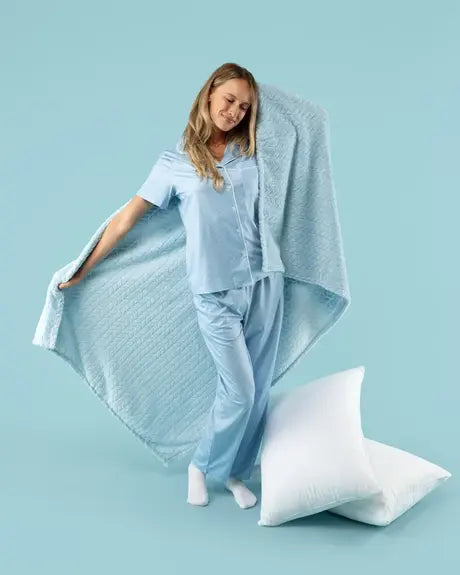 Creator unfurling a light blue EverSnug blanket beside pillows