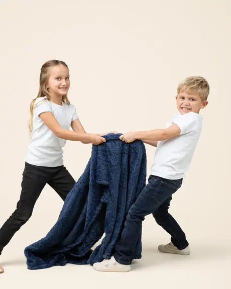 Two kids playing tug-of-war with a navy EverSnug blanket