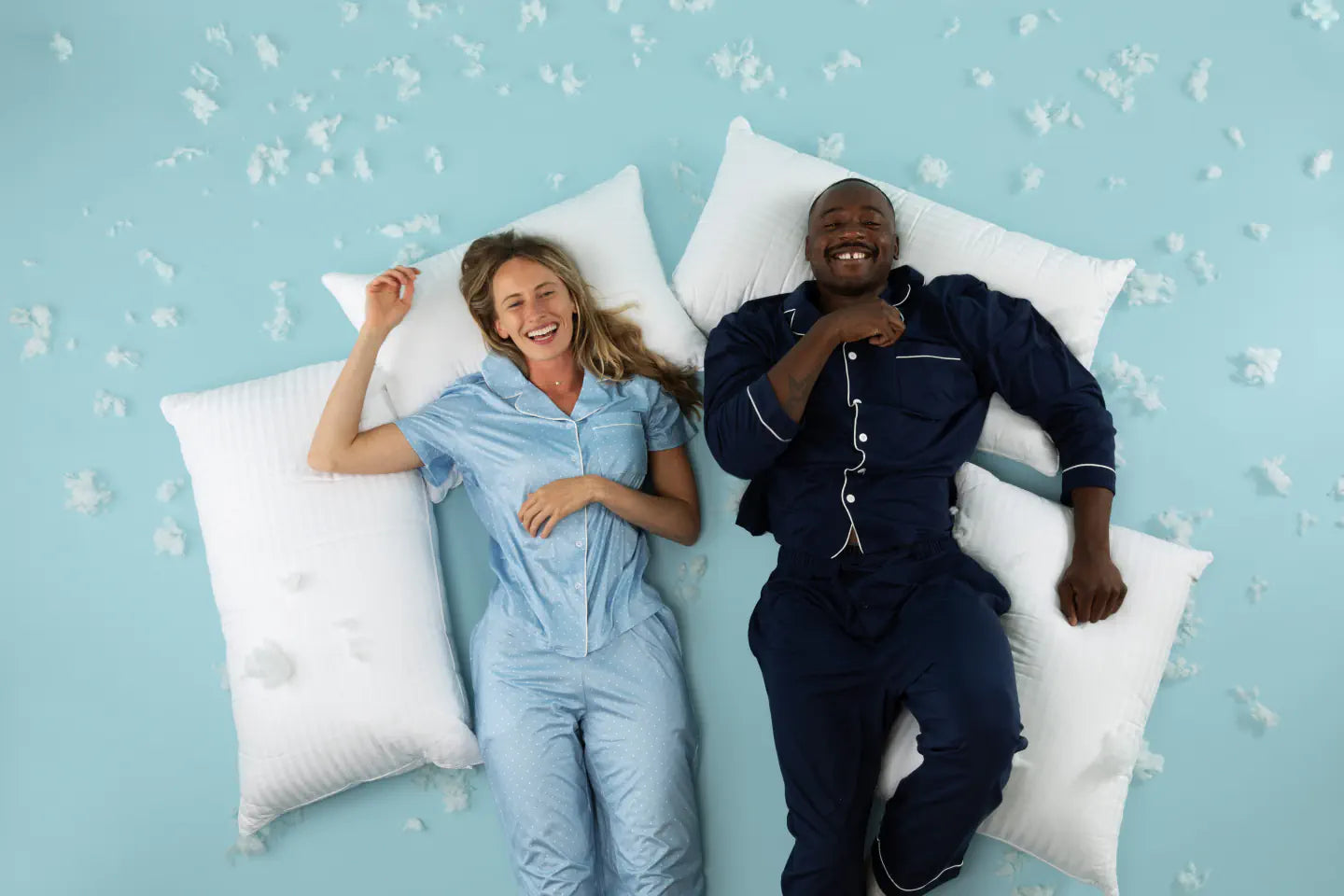 Two adults seated with EverSnug pillows and a blanket on a blue studio set