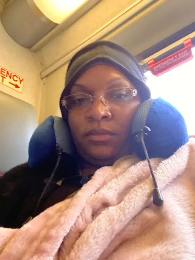 A train passenger wearing glasses uses a navy pillow and a pink EverSnug blanket