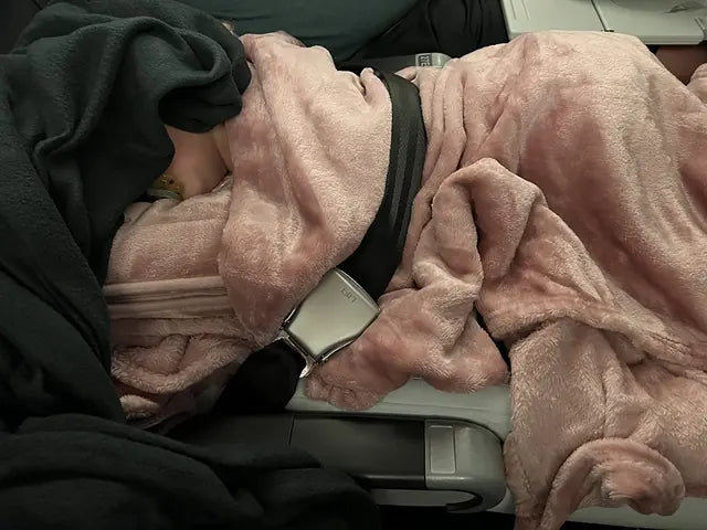Two children sleep across airplane seats under pink and dark grey EverSnug blankets