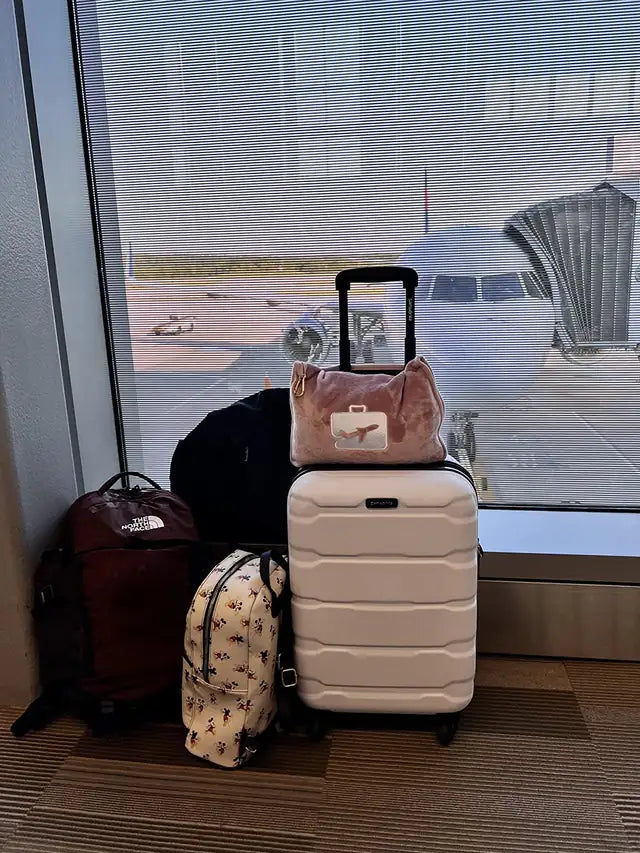 A pink EverSnug travel pillow sits on a cream suitcase in front of an airport window and airplane